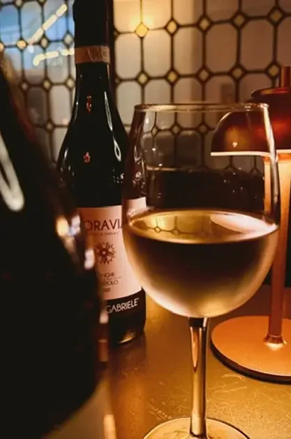 Glass of white wine and Italian red on a gold table inside Rockwell & Rose – styled against warm tile and table lighting.