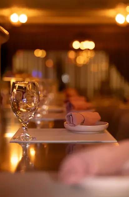 Polished place setting with rose napkin fold at the bar – intimate lighting and curved glassware detail.