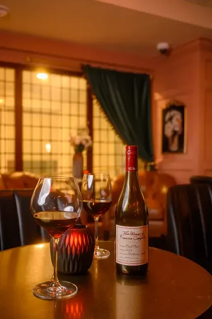 Francis Coppola Pinot Noir 2023 with two glasses on a candlelit table inside Rockwell & Rose, Philadelphia – plush seating and soft pink walls in the background.