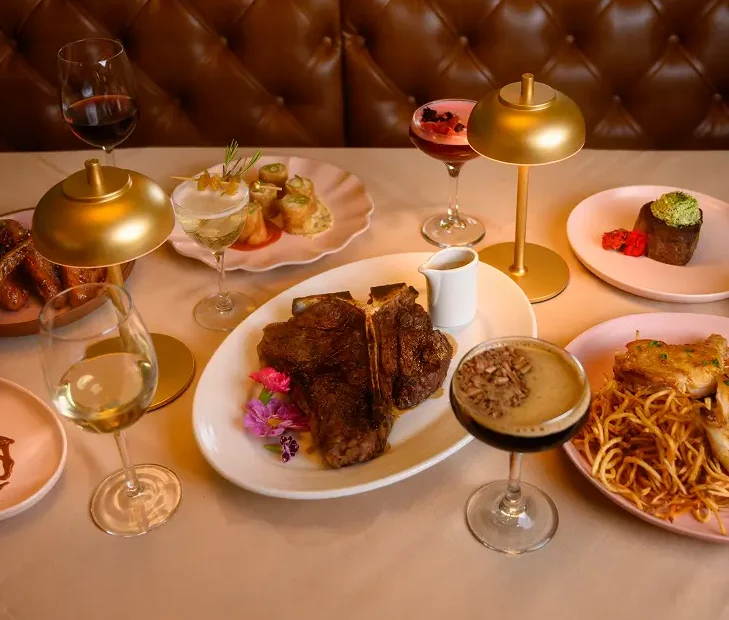 Private dining setup at Rockwell & Rose featuring a Dry-Aged Ribeye, pasta, and espresso – under warm gold lighting and leather seating.