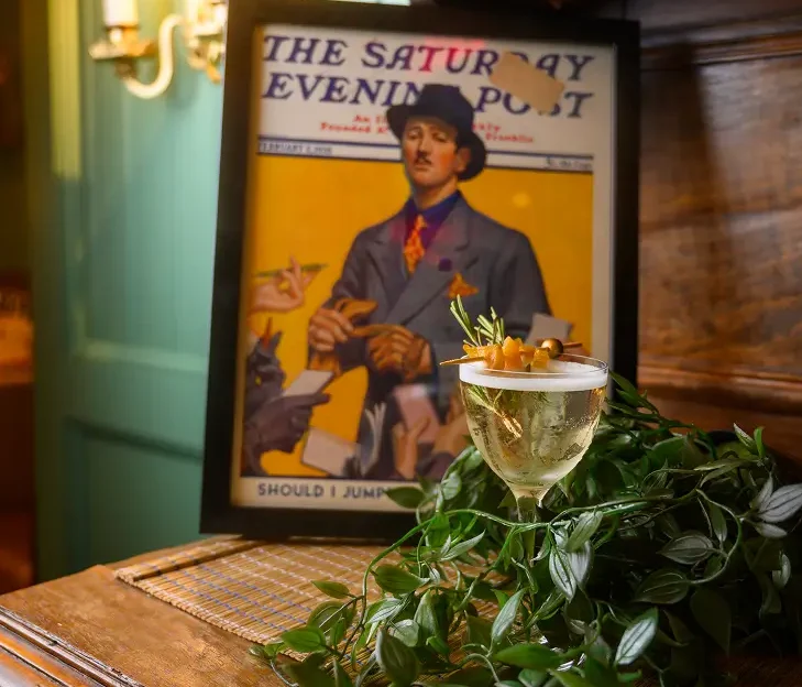 House cocktail garnished with herbs and olives, photographed in front of The Saturday Evening Post cover – a nod to The Curtis building’s history.