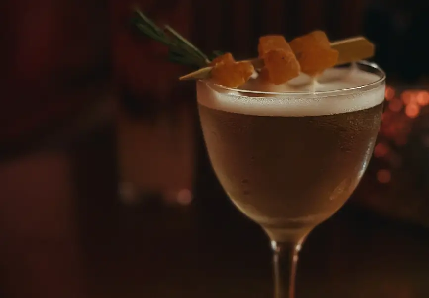 Signature house cocktail from the Rose side of the menu, garnished with rosemary and candied fruit – part of the seasonal drinks program.