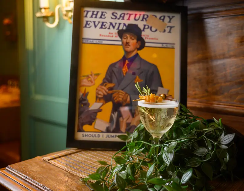 House cocktail garnished with herbs and olives, photographed in front of The Saturday Evening Post cover – a nod to The Curtis building’s history.