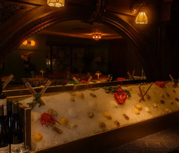 Fresh oysters and shellfish displayed on ice at the Rockwell & Rose raw bar – beneath carved wood and moody overhead lighting.